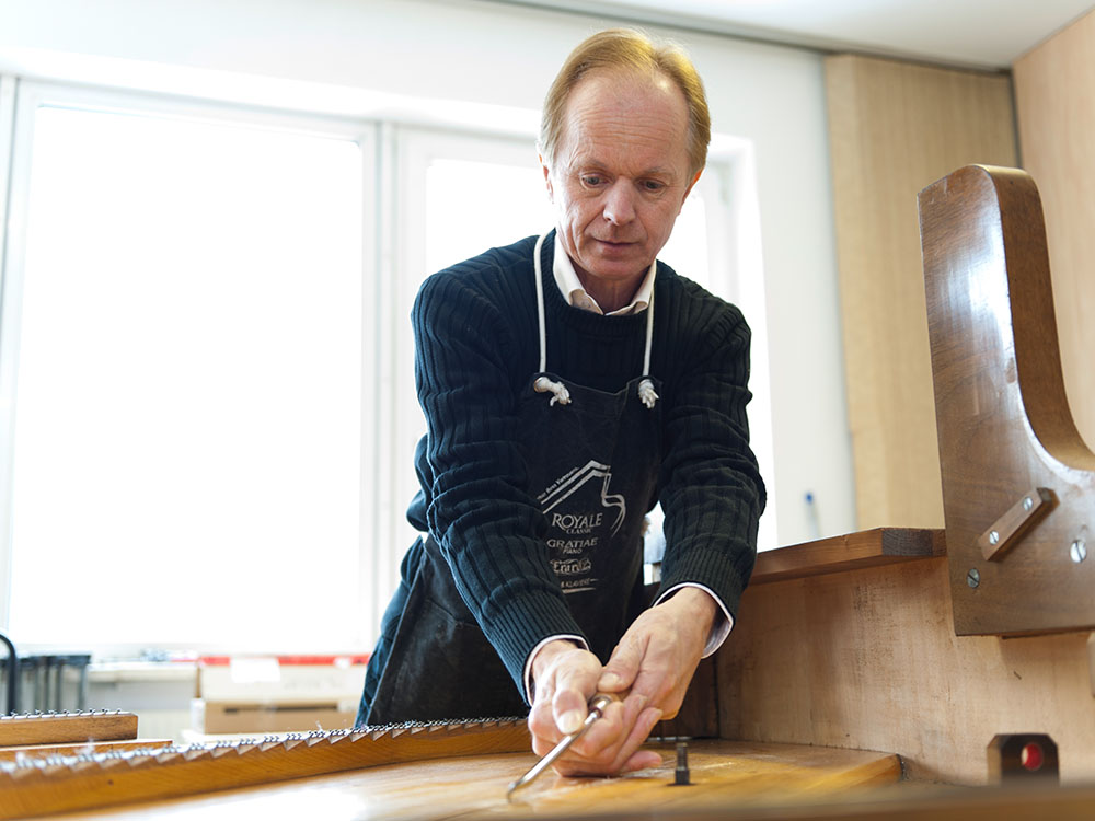 Herbert Vogel hält ein Stemmeisen in der Hand und bearbeitet damit das Innenleben eines Klaviers.