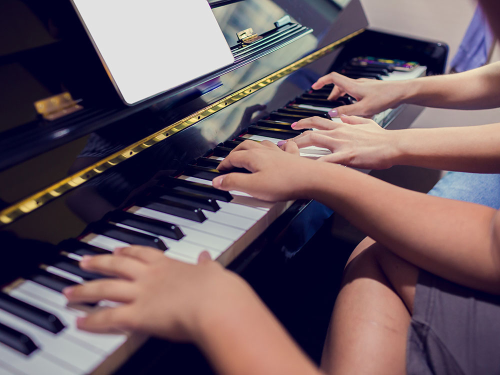 Vier Hände, die auf einer Klaviertastatur spielen