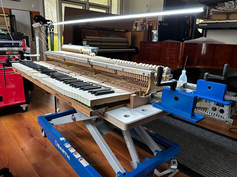 Die Mechanik eines Klaviers liegt auf einer Werkbank, umgeben von einem Klavier, einem Flügel und einer High-Tech-Werkbank.
